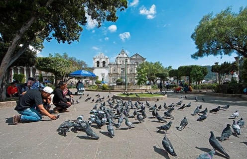Parque Centroamérica or Parque Central, a Mayan woman in traditional clothing feeds pigeons, in the