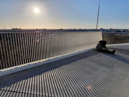 A person sitting alone on a railing with a view of an urban landscape at sunset, abstract, stripes,