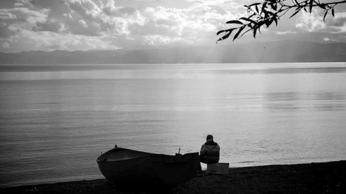 Lonely person on lake shore with boat and calm water surface in black and white, Ohrid Lake, North