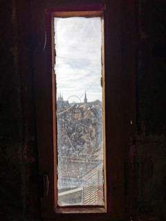 View through a narrow window of a city with church towers and a Ferris wheel under a cloudy sky