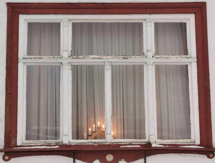 Rustic window with red wooden frame and candles inside, creates a cozy evening mood