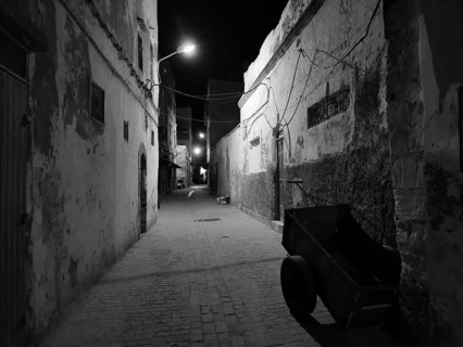 Abandoned old alley in nighttime darkness, faintly lit by black and white lanterns, Essaouira,