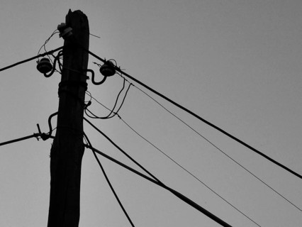 Close-up of an old wooden power pole with several wires against the sky, black and white, Berat,