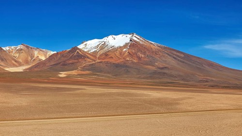 Majestic snow-capped mountain in front of a vast, sandy desert landscape, The landscape of the