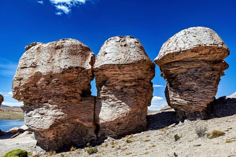 Three monumental rocks stand proudly in a dry desert landscape under clear blue skies, The