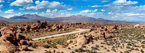 Wide panoramic landscape with large rocks, a dusty desert and mountains under a cloudy sky, The