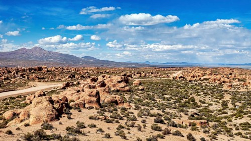 Desert landscape with a road leading through rocks and mountains, under a sky with clouds, The