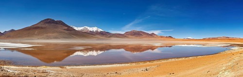 Extensive landscape with reflecting lake and snow-capped mountains under bright skies, Laguna