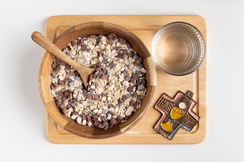 Wooden bowl with cereal and a cross on a wooden board with water, fasting