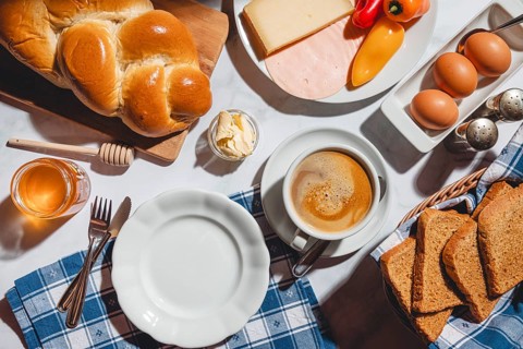 Breakfast with toast, stollen, honey, cheese, ham, coffee, butter, peppers and eggs on a table