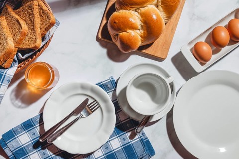 Breakfast items such as toast, stollen, eggs and honey on a white table