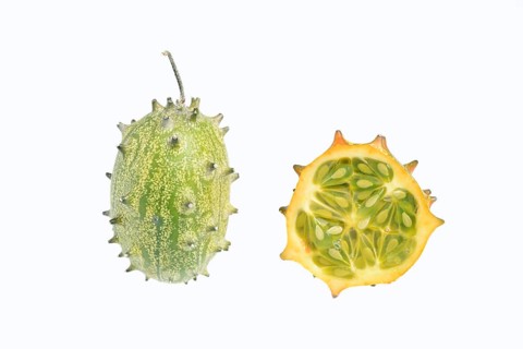 Horned cucumber, kiwano or horned melon (Cucumis metuliferus), whole and sliced fruit on a white