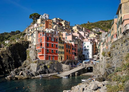 Colourful houses under blue sky, view of the fishing village of Riomaggiore, boats in the harbour,