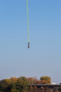 Female bungee jumper in midair with her ankles tied to a long yellow elastic bungee jumping cord,