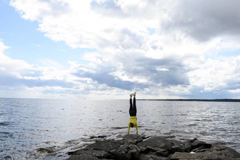 Young woman girl doing a handstand on rocks at Lake Vänern under cloudy sky, Värmlands län, Sweden