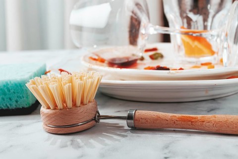 Dishes are stacked on a kitchen counter with food remnants after a meal. A cleaning brush and