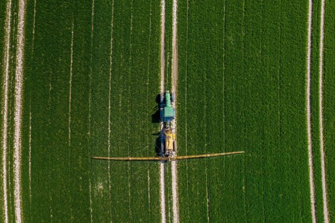 Aerial view over agricultural trailed field sprayer pulled by tractor spraying crop on farmland,
