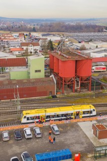 Aerial view of an industrial area with a yellow train and large red buildings, taking the Hermann