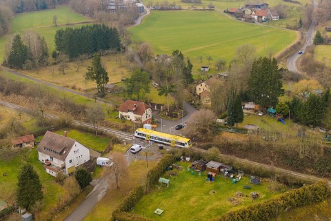 Rural scene with yellow train on rails, surrounded by trees and houses in the countryside,