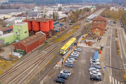 Railway station with yellow train in a rural area, surrounded by cars and buildings, acceptance of