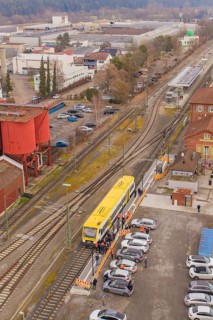 Yellow train at a train station surrounded by vehicles and buildings from a bird's eye view, taking