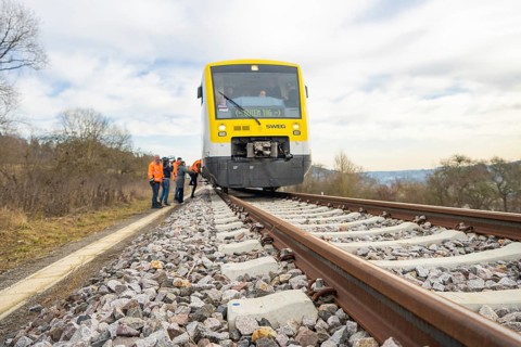 A train travels through a rural landscape with waiting passengers, taking the Hermann Hesse