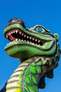 Green dragon with big teeth and long red tongue against blue sky background, Fun Show traveling