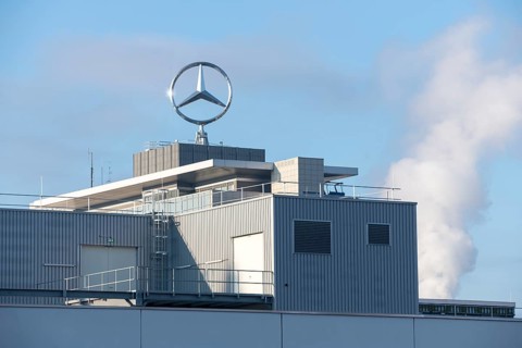 Close-up of a modern building with Mercedes logo and clouds of smoke in the background, blue sky,