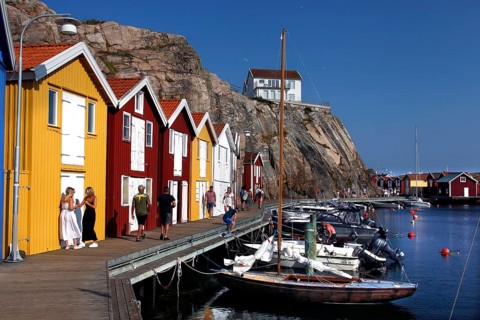 Lively harbor scene with colorful boathouses and walkers along the promenade, Smögen, Västra
