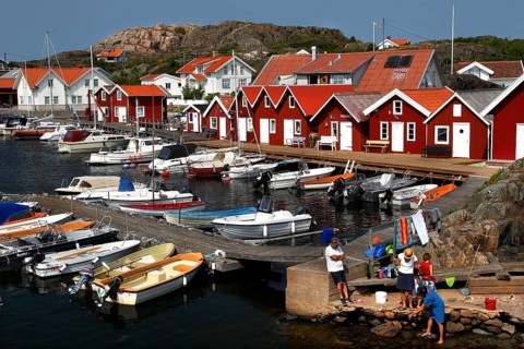 Red wooden houses on a lively harbour full of boats in idyllic surroundings, Klädesholmen, Västra