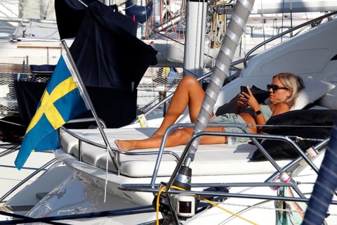 Woman relaxing on a sailboat with Swedish flag in harbor, Smögen, Västra Götaland, Sweden