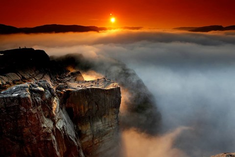 A golden horizon spreads over the sea of clouds and the mighty cliffs of Preikestolen,