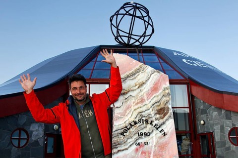 Happy person in front of the distinctive symbol of the Arctic Circle, zero