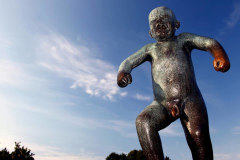 Bronze statue of an angry child against a blue sky in Vigelandsparken, Oslo, Norway
