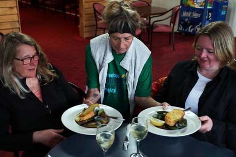 Two woman are served plates of mussels at a restaurant table by a waitress, Havelock Hotel,