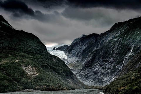 The Franz Josef Glacier with dramatic skies and steep, forested mountain slopes, Franz Josef, West