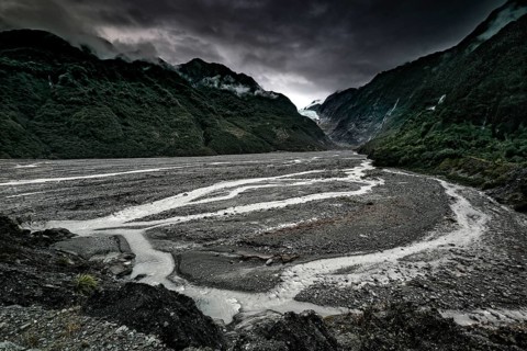Franz Josef glacier flanked by an extensive riverbed and under dark clouds, Franz Josef, West