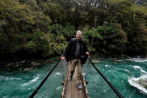 Person standing on a suspension bridge over a fast river, Fjordland National Park, New Zealand