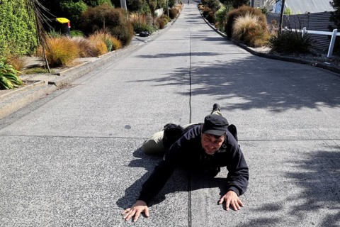A person humorously lies on steep Baldwin Street in Dunedin, Dunedin, zero, New Zealand