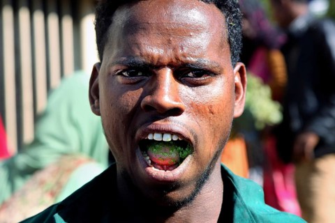 Man with khat leaves in his mouth smiles during lively market activity, Awaday, Afar, Ethiopia
