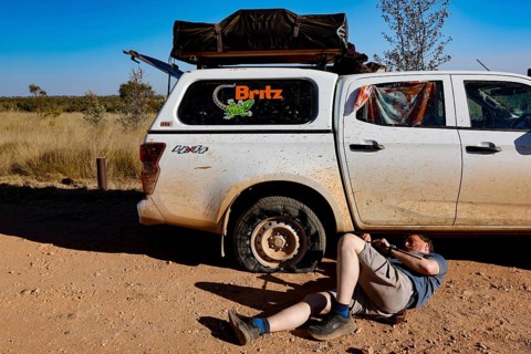 Person repairs flat tire next to a car in Purnululu National Park, Purnululu National Park, Western