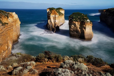 Impressive rocks rise from a calm sea under a blue sky, zero