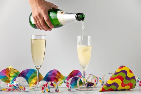 Sparkling wine is filled into glasses surrounded by colorful streamers, carnival
