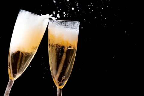 Two glasses of champagne touching each other with splashes against a dark background
