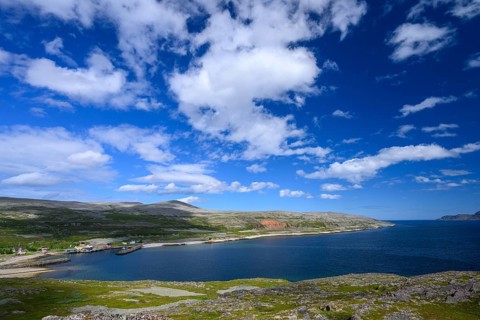 Green meadows on the banks of Syltefjord with clouds in the blue sky, landscape with a lake and