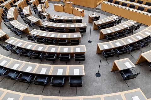 Plenary hall deserted with the seats of deputies and the government bank. Behind it is the coat of