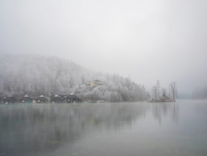 View across Königssee to boathouses, Christlieger island and frozen trees in fog, Schönau am