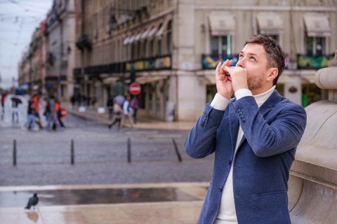 Man musician in a blue blazer and white sweater playing blues on a harmonica with eyes closed,