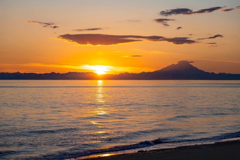 View of Cook Inlet on white mountain peaks of Mount Redoubt at sunset, picturesque golden light of
