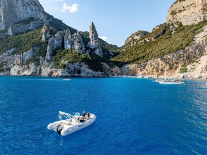 Motor boat off picturesque rocky coast, cliffs with L'Aguglia pinnacle, blue sea and Cala Goloritzé